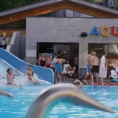Rodzina szaleje na zjeżdżalni w hotelu z aquaparkiem w górach. Woda pluska, a słońce świeci.