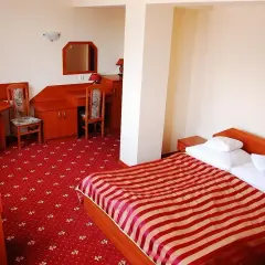 Pokój w hotelu jurajskim Kraków: łóżko z czerwono-białą pościelą, dywan, biurko i stolik.
