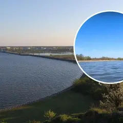 Rozległy sztuczny zbiornik wody z widocznym w oddali miastem i mostem. W okręgu zbliżenie na spokojną taflę wody i linię brzegową.