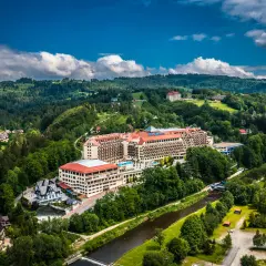 Widok z lotu ptaka na duży hotel Gołębiewski otoczony zielonymi wzgórzami i rzeką.