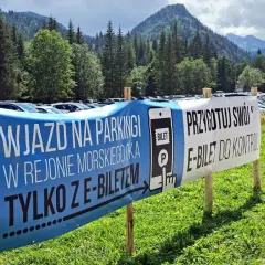 Wjazd na parking w Morskim Oku tylko z e-biletem. Przygotuj swój e-bilet do kontroli. Tło to góry i las.