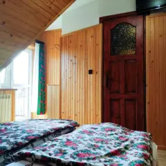 Pokój w pensjonacie Janina z Górali. Dwa łóżka z kwiecistą pościelą, drewniane ściany i drzwi.