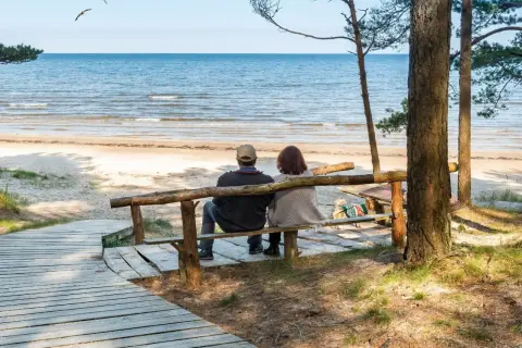 Para odpoczywa na ławce przy plaży, ciesząc się widokiem morza. Idealne miejsce na relaks w sanatorium nad morzem.
