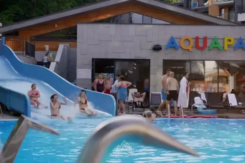 Rodzina szaleje na zjeżdżalni w hotelu z aquaparkiem w górach. Woda pluska, a słońce świeci.