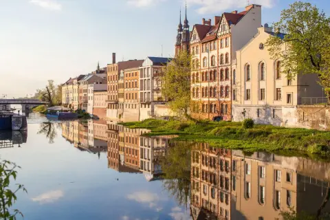 Nad rzeką w najmniejszym województwie w Polsce, w słoneczny dzień, odbijają się w wodzie zabytkowe kamienice.