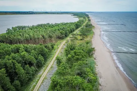 Malownicza trasa rowerowa R10 wzdłuż lasu i plaży nad Bałtykiem. W oddali widać jezioro i farmę wiatraków.