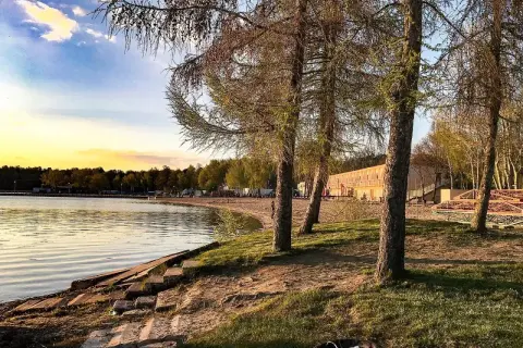Zachód słońca nad jeziorem, plaża i budynek z tarasem. Skorzęcin atrakcje czekają na turystów.