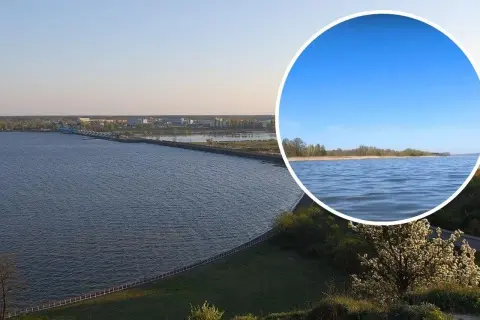 Rozległy sztuczny zbiornik wody z widocznym w oddali miastem i mostem. W okręgu zbliżenie na spokojną taflę wody i linię brzegową.