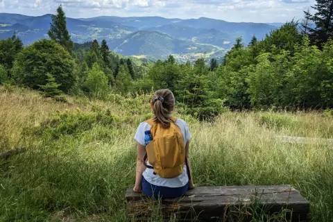 Kobieta z plecakiem odpoczywa na ławce, podziwiając malowniczy krajobraz górski. Idealne miejsce na wędrówkę po piwniczna zdrój szlaki.