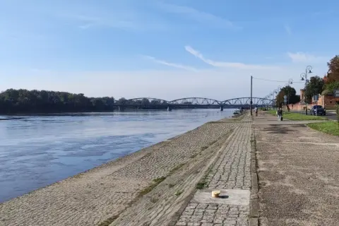 Spacerując po urokliwych trasach rowerowych Torunia, podziwiamy Wisłę i zabytkowy most.