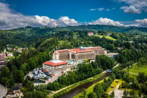 Widok z lotu ptaka na duży hotel Gołębiewski otoczony zielonymi wzgórzami i rzeką.