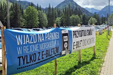 Wjazd na parking w Morskim Oku tylko z e-biletem. Przygotuj swój e-bilet do kontroli. Tło to góry i las.