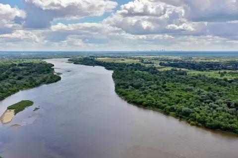 Szeroka Wisła, najdłuższa rzeka w Polsce, płynie przez zielone tereny z widoczną w oddali panoramą miasta.