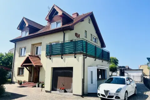 Jasny dom z balkonem i napisem "Ria" oferuje kwatery nad morzem. Biały samochód zaparkowany przed posesją.