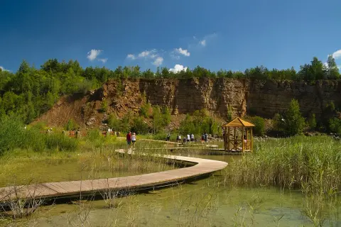Malowniczy park w Jaworznie z drewnianą kładką wijącą się nad wodą, skalnym zboczem i altanką.