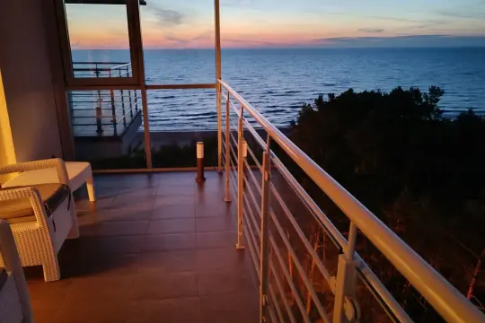 Dziwnówek noclegi z widokiem na morze. Balkon z białymi meblami i widokiem na spokojne morze o zachodzie słońca.
