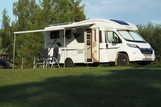 Białe przyczepy kempingowe nad morzem, rozłożony przedsionek, stolik i krzesła na trawie. Idealne miejsce na wakacje.