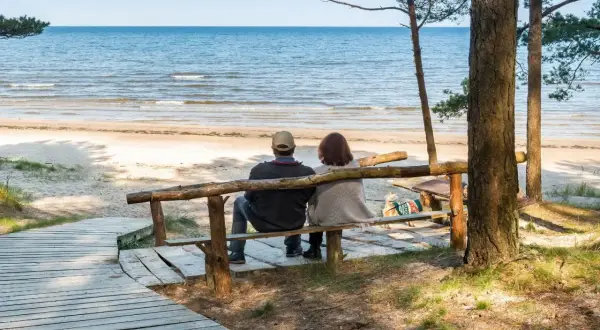 Para odpoczywa na ławce przy plaży, ciesząc się widokiem morza. Idealne miejsce na relaks w sanatorium nad morzem.