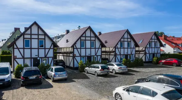 Tanie domki nad morzem w stylu szachulcowym, z parkingiem i samochodami.