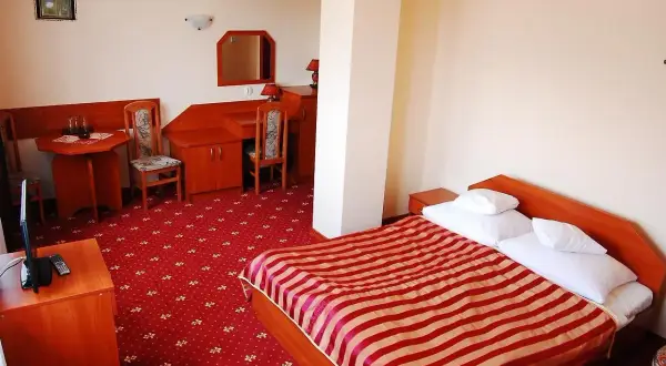 Pokój w hotelu jurajskim Kraków: łóżko z czerwono-białą pościelą, dywan, biurko i stolik.