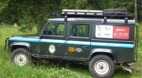Samochód TOPR w górach, z napisem "Tatrzańskie Ochotnicze Pogotowie Ratunkowe" i numerem ratunkowym.