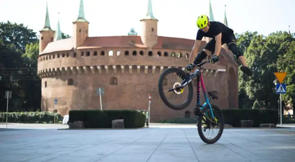 Wykonuje trik na rowerze po krakowsku, z zabytkowym Barbakanem w tle.