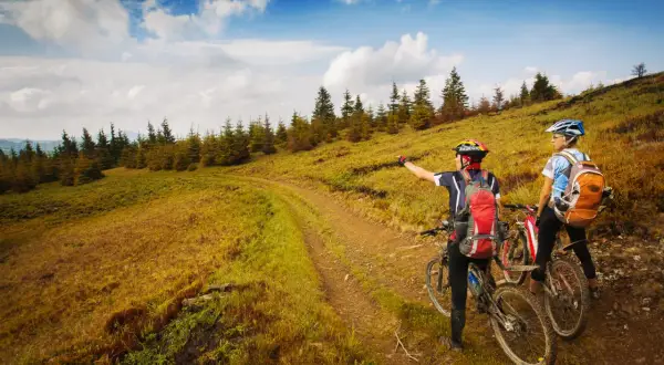 Dwie osoby na rowerach górskich zatrzymały się na szlaku, by podziwiać widok. Jedna z nich wskazuje drogę. To wspaniała przygoda rowerem po górach!