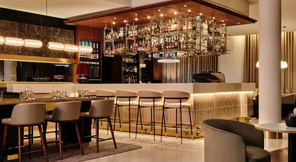 Elegancki bar w hotelu Radisson Blu Kraków. Wnętrze z bogatą ekspozycją alkoholi, wygodnymi hokerami i stylowym oświetleniem.