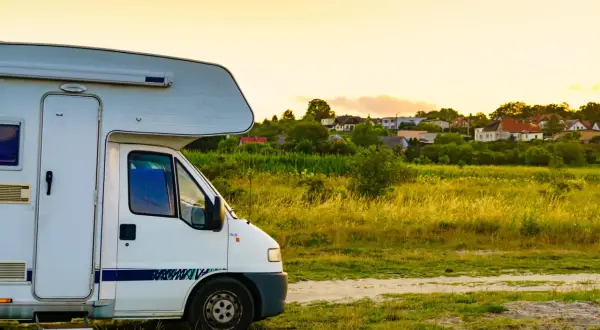 Biały kamper na tle wsi. Zastanawiasz się, ile kosztuje wypożyczenie kampera na wakacje?