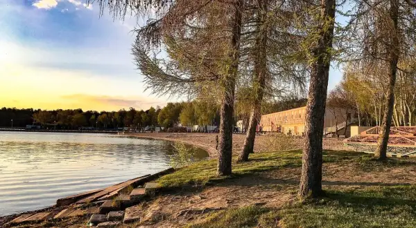 Zachód słońca nad jeziorem, plaża i budynek z tarasem. Skorzęcin atrakcje czekają na turystów.