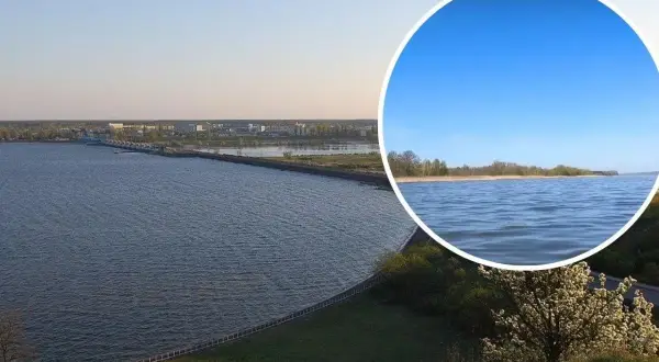 Rozległy sztuczny zbiornik wody z widocznym w oddali miastem i mostem. W okręgu zbliżenie na spokojną taflę wody i linię brzegową.