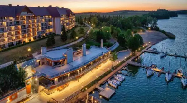 Zachód słońca nad jeziorem, gdzie cumują łodzie przy Hotelu Gołębiewski Mikołajki. Malowniczy widok na architekturę i wodę.