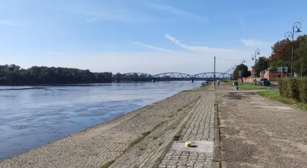Spacerując po urokliwych trasach rowerowych Torunia, podziwiamy Wisłę i zabytkowy most.