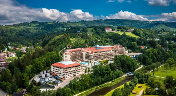 Widok z lotu ptaka na duży hotel Gołębiewski otoczony zielonymi wzgórzami i rzeką.