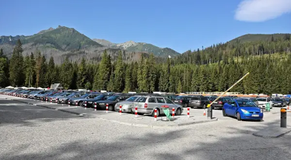 Parking pod Morskim Okiem, pełen samochodów, z górami i lasem w tle.