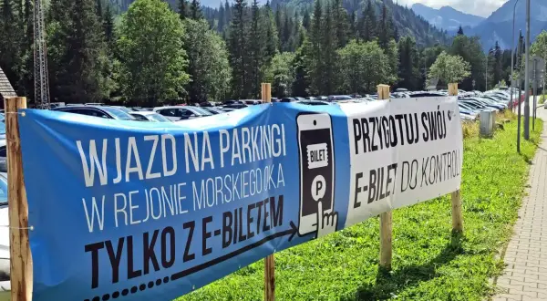 Wjazd na parking w Morskim Oku tylko z e-biletem. Przygotuj swój e-bilet do kontroli. Tło to góry i las.