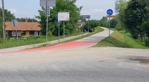 Czerwony pas wyznacza nowe trasy rowerowe w Tarnowie. W tle domki i zielone drzewa.