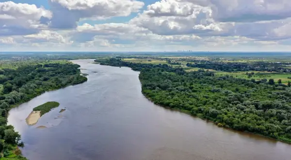 Szeroka Wisła, najdłuższa rzeka w Polsce, płynie przez zielone tereny z widoczną w oddali panoramą miasta.