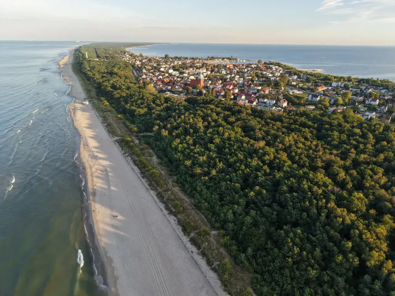 Majówka nad morzem: szeroka, piaszczysta plaża, szum fal i zielony las otaczający urokliwe domki. Idealne miejsce na odpoczynek.