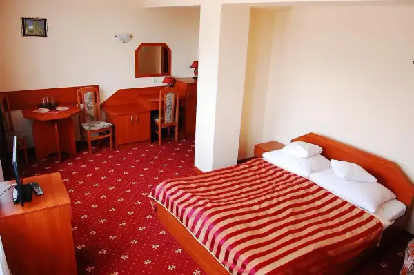 Pokój w hotelu jurajskim Kraków: łóżko z czerwono-białą pościelą, dywan, biurko i stolik.