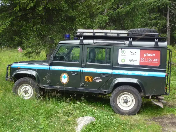 Samochód TOPR w górach, z napisem "Tatrzańskie Ochotnicze Pogotowie Ratunkowe" i numerem ratunkowym.