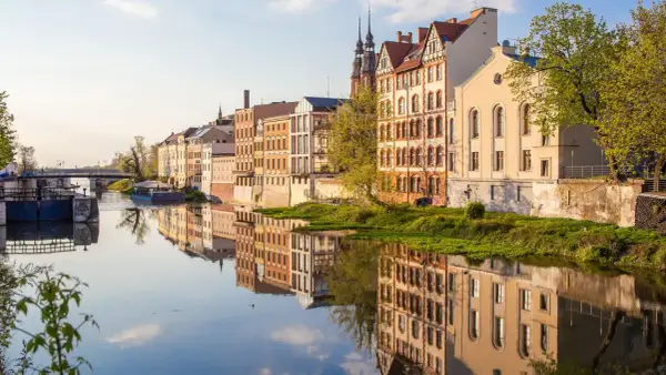 Nad rzeką w najmniejszym województwie w Polsce, w słoneczny dzień, odbijają się w wodzie zabytkowe kamienice.
