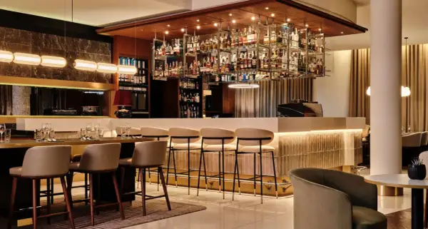 Elegancki bar w hotelu Radisson Blu Kraków. Wnętrze z bogatą ekspozycją alkoholi, wygodnymi hokerami i stylowym oświetleniem.