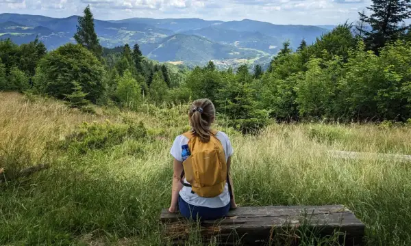 Kobieta z plecakiem odpoczywa na ławce, podziwiając malowniczy krajobraz górski. Idealne miejsce na wędrówkę po piwniczna zdrój szlaki.