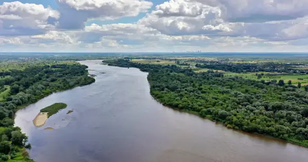 Szeroka Wisła, najdłuższa rzeka w Polsce, płynie przez zielone tereny z widoczną w oddali panoramą miasta.