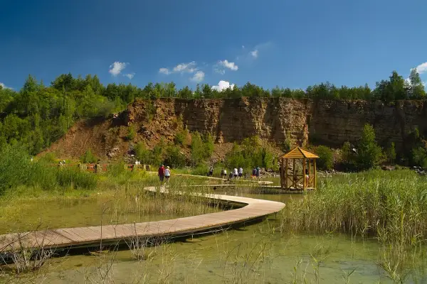 Malowniczy park w Jaworznie z drewnianą kładką wijącą się nad wodą, skalnym zboczem i altanką.